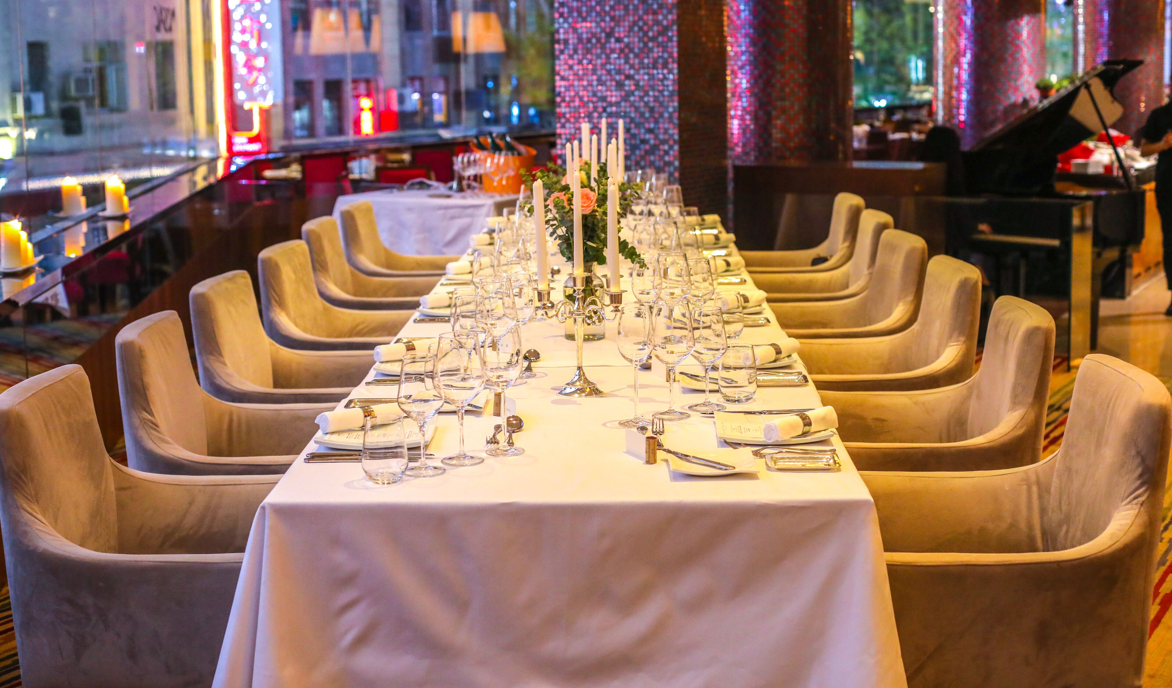 A long dining table set with multiple chairs, candles, and glassware, indicating a formal dining setup.
