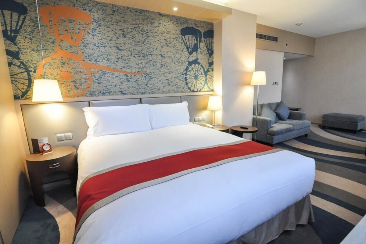 A hotel room with a large bed, a sofa, a chair, and a wall with a bicycle mural.