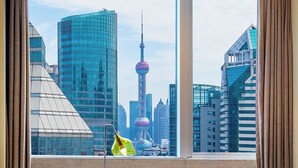 A view of a cityscape through a window with curtains, featuring modern buildings and a prominent tower.