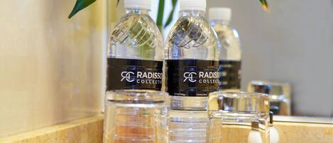 A bathroom counter with three bottles of Radisso Collection drinking water, a small glass, and a bottle of body lotion.