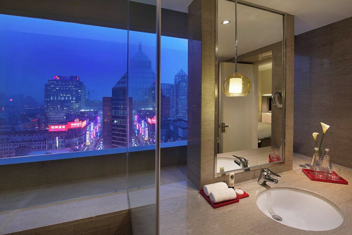 A modern bathroom with a large mirror, a sink, and a glass-enclosed window offering a city view.