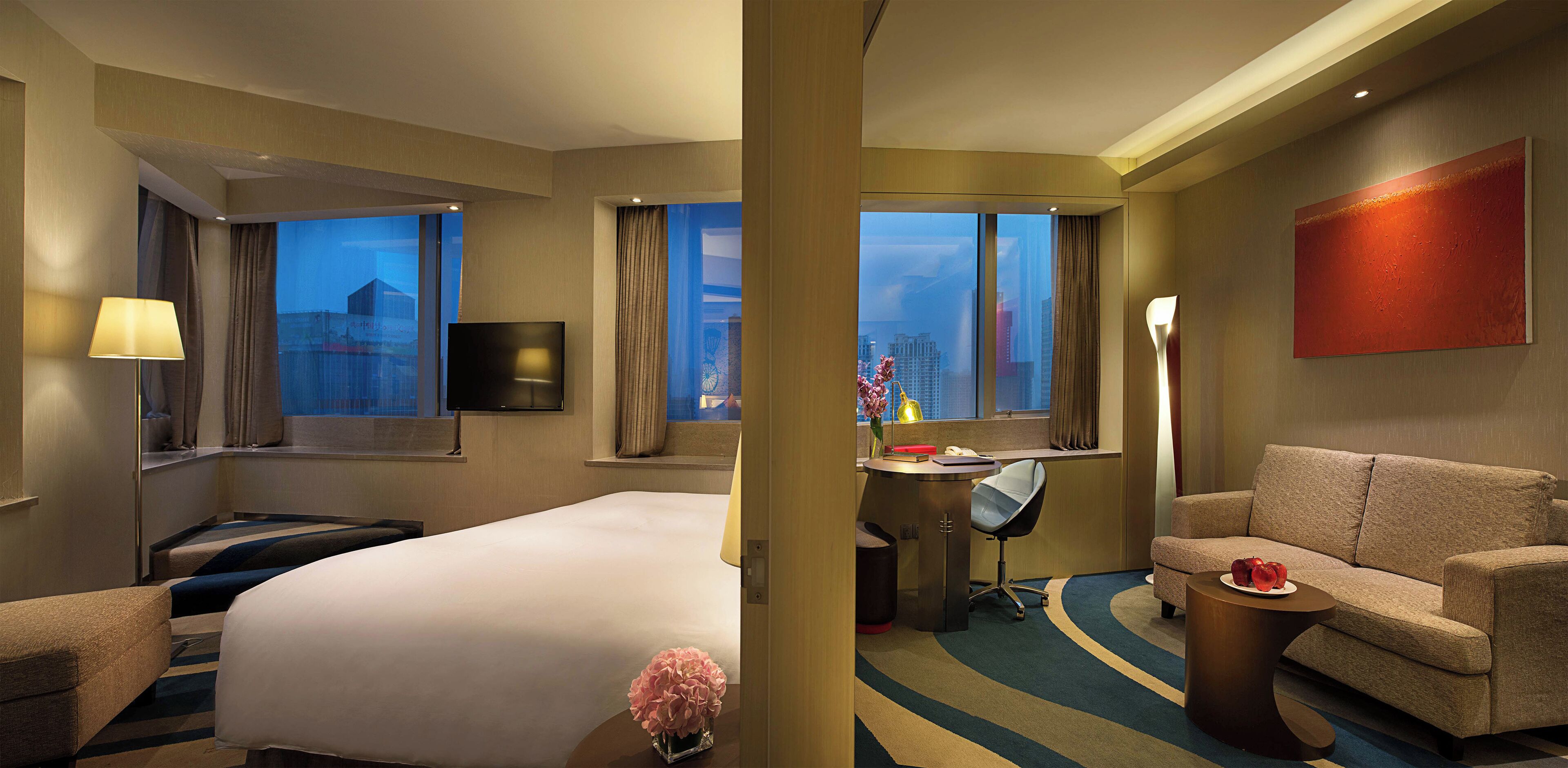 Habitación de hotel con una cama grande, un escritorio con una silla, un sofá y un televisor en la pared.