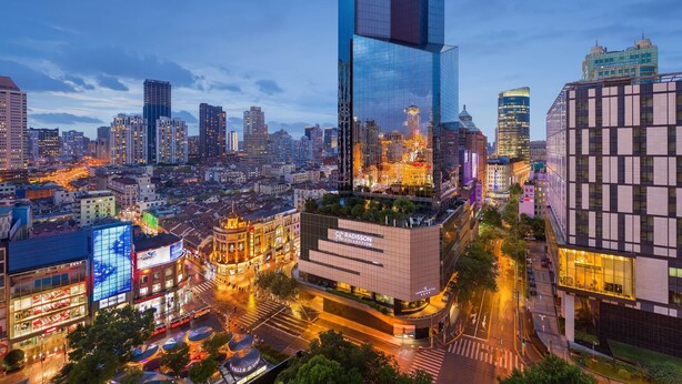 A modern cityscape with a prominent skyscraper featuring a large illuminated sign.