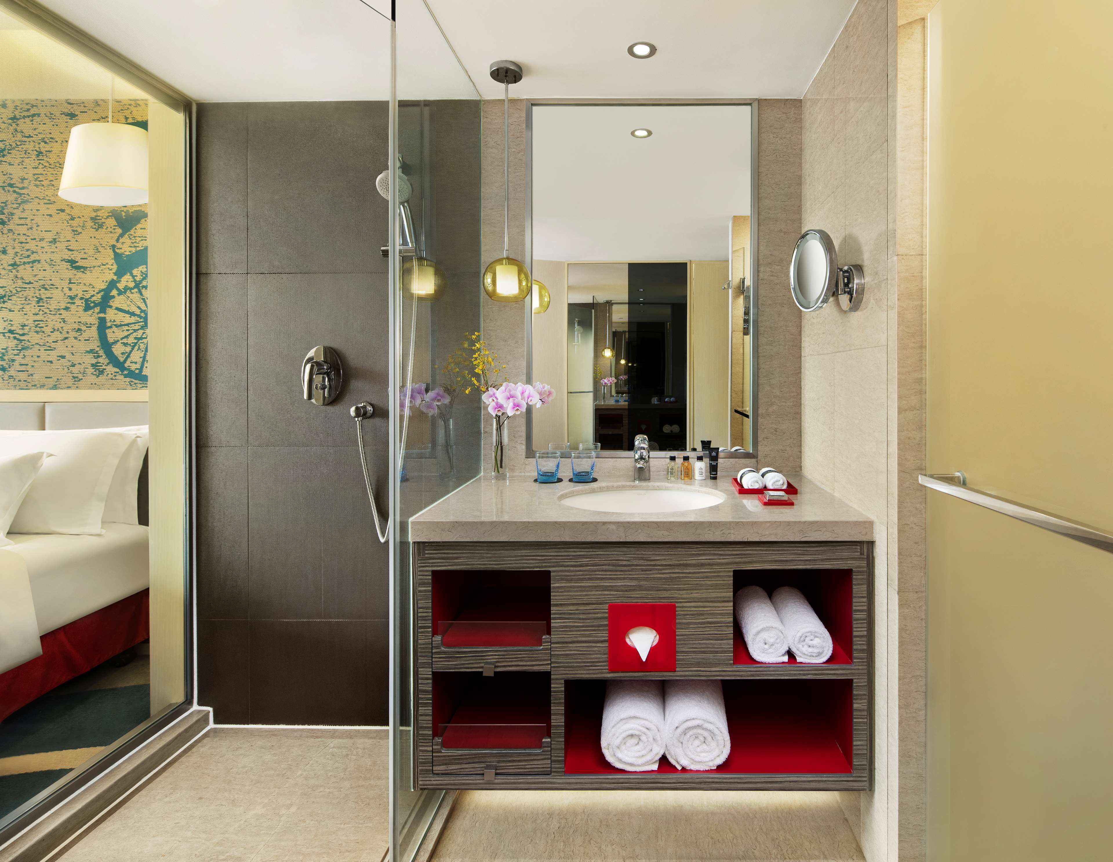 A modern bathroom with a glass shower enclosure, a vanity with a mirror, and a built-in shelf with towels.