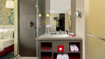 A modern bathroom with a glass shower enclosure, a vanity with a mirror, and a built-in shelf with towels.