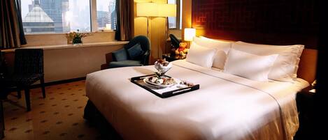 Ein Hotelzimmer mit einem großen Bett, einem Schreibtisch mit Lampe, einem Sessel und einem Fenster mit Blick auf Gebäude.