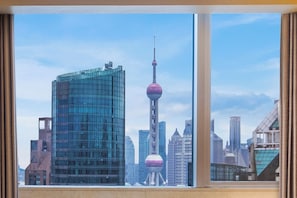 Vista de un paisaje urbano a través de una ventana, con edificios modernos y una torre distintiva con un mirador esférico.