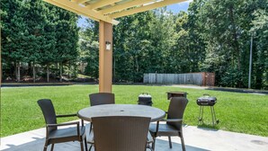 Een terras buiten met een ronde tafel en vier stoelen, een barbecue en een overdekt gebied met een pergola.