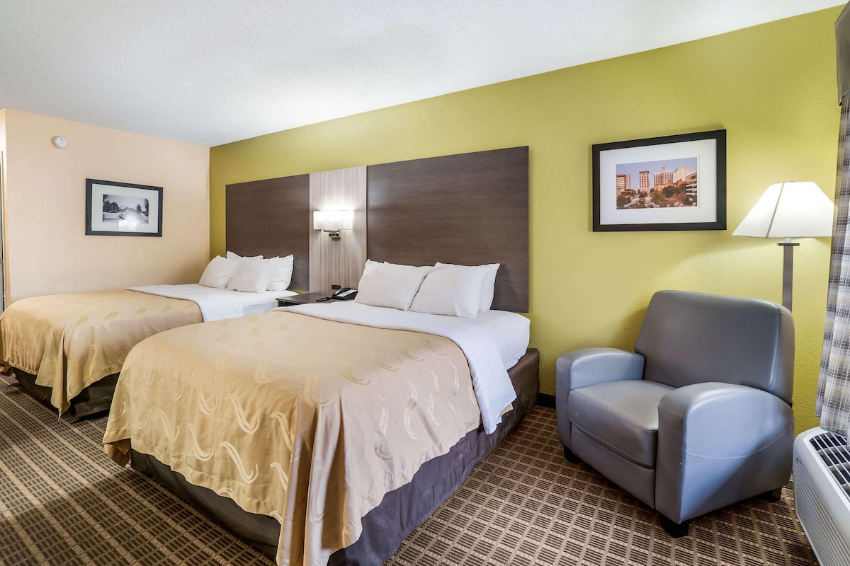 A hotel room with two beds, a desk, a chair, a lamp, and a picture on the wall.