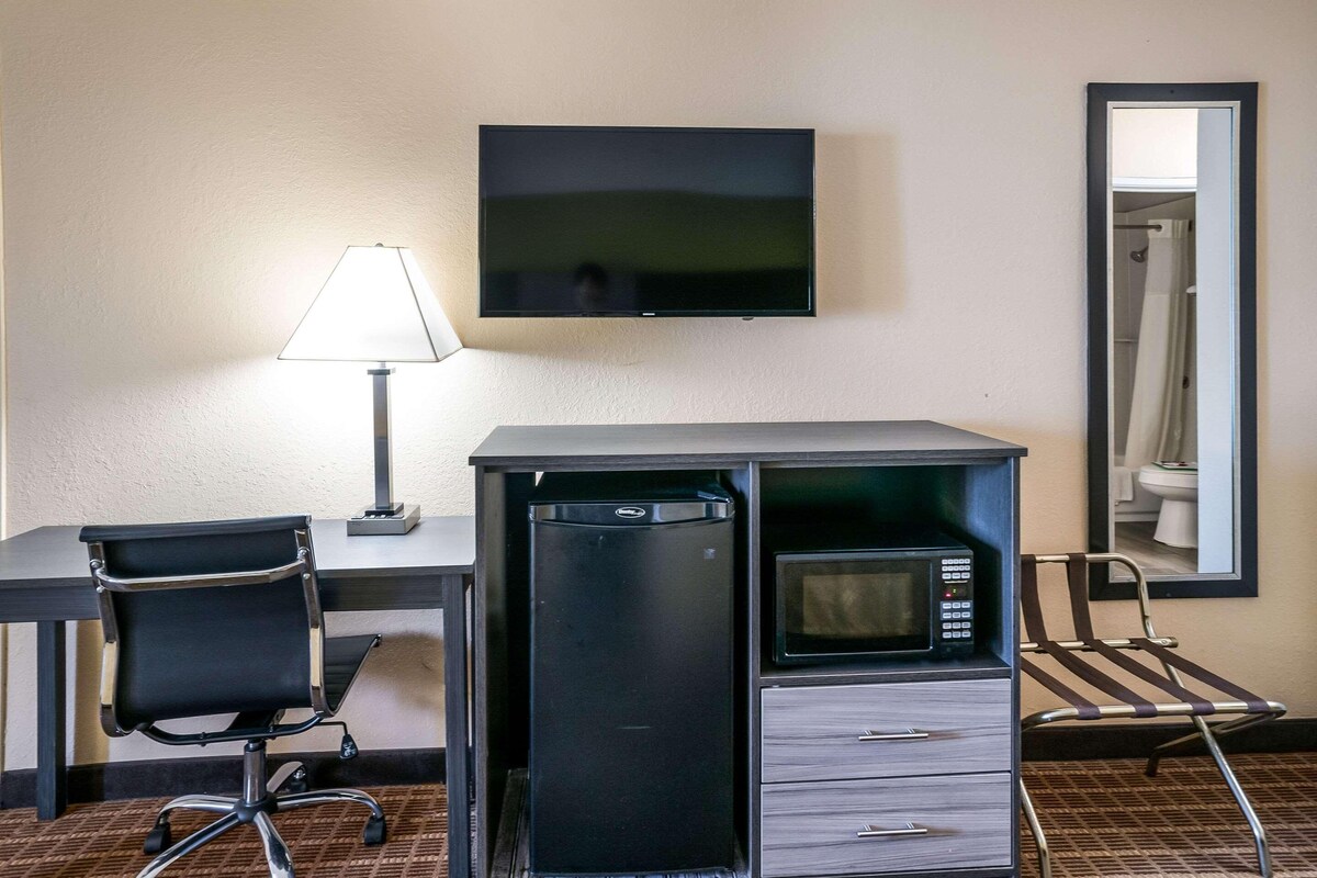Habitación de hotel con escritorio, una silla, televisor de pantalla plana montado en la pared, microondas y espejo.
