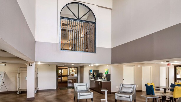 Een ruime lobby met een hoge plafond, een trap en een zithoek met stoelen en tafels.