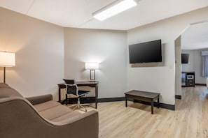 A hotel room with a sofa, a desk with a chair, a TV mounted on the wall, and a small table. - Clarion Pointe Louisville East (Louisville)
