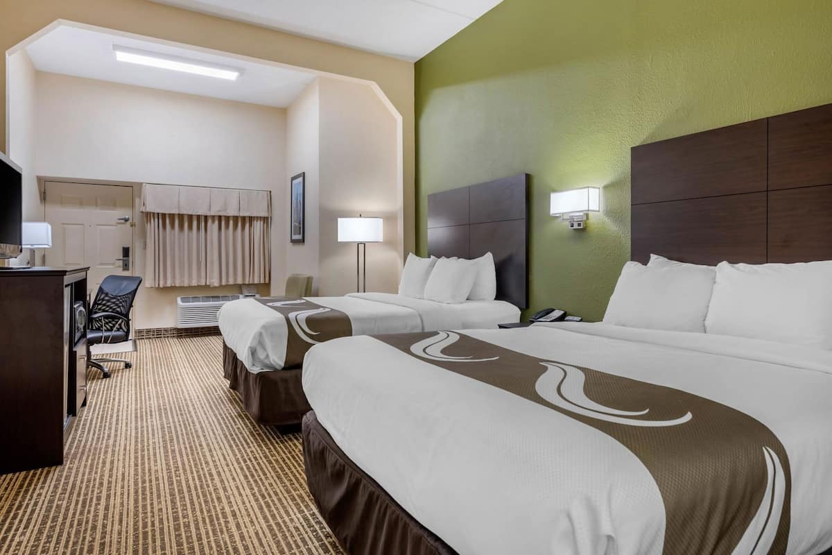 Una habitación de hotel con dos camas, un escritorio, una silla, una lámpara y un teléfono.