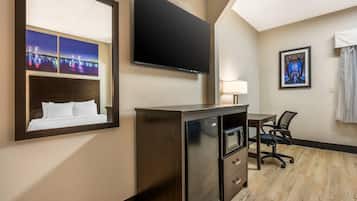 A hotel room with a bed, a desk with a chair, a television mounted on the wall, and a framed picture.