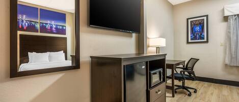 Une chambre d’hôtel avec un lit, un bureau et une chaise, un téléviseur fixé au mur et un tableau encadré.