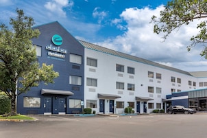 Un hotel de diseño moderno, con un logo destacado en la fachada, varios accesos y un área de estacionamiento.