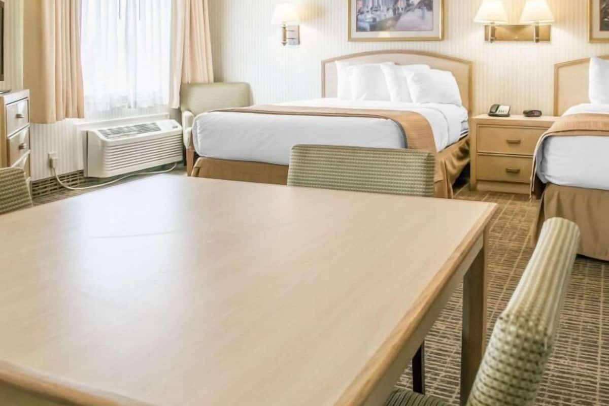 Habitación de hotel con cama, mesitas de noche, escritorio, silla, lámpara, un cuadro en la pared y ventana con cortinas.