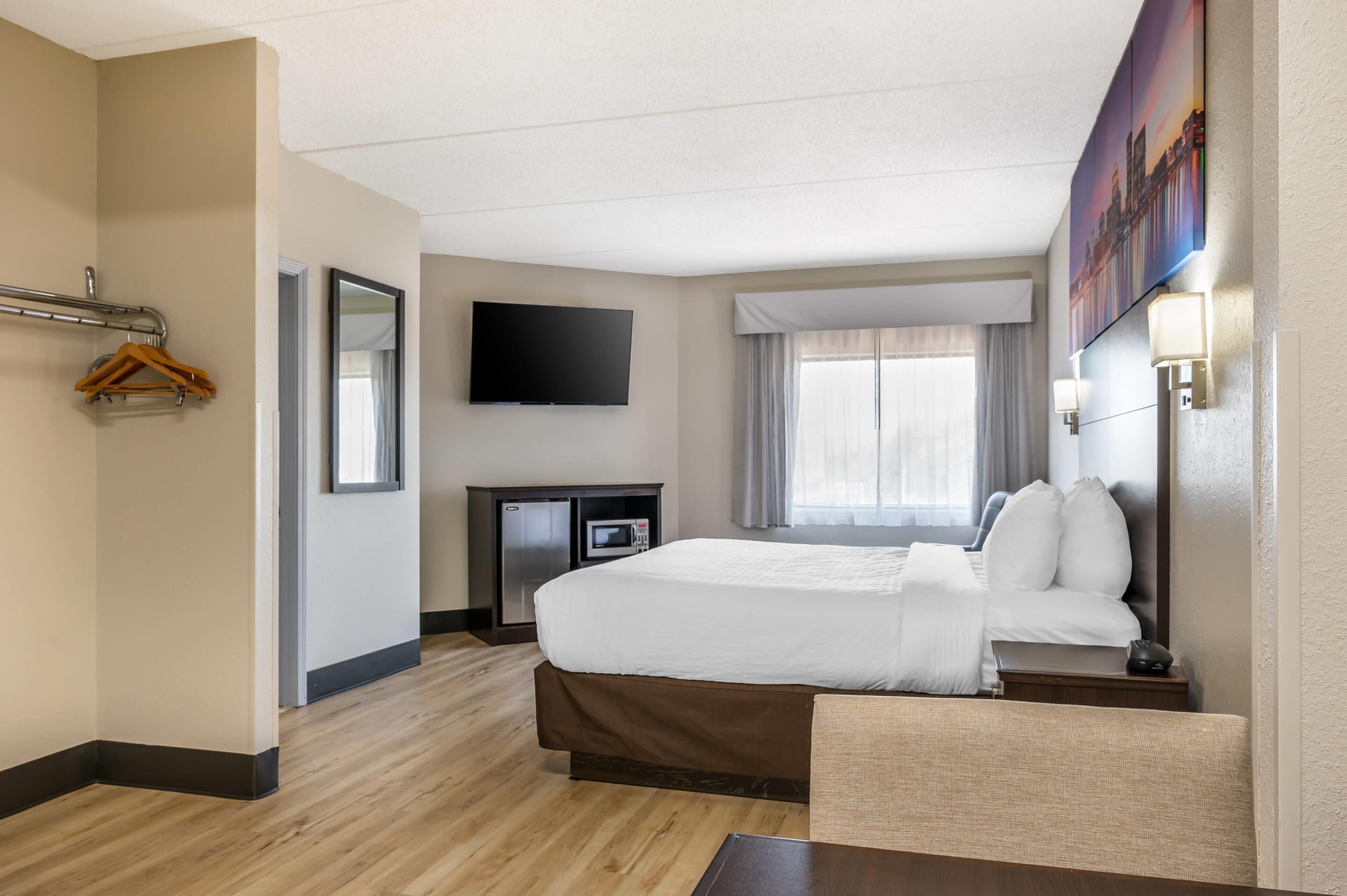 Habitación de hotel con cama, escritorio, televisor de pantalla plana, microondas y ventana con cortinas.