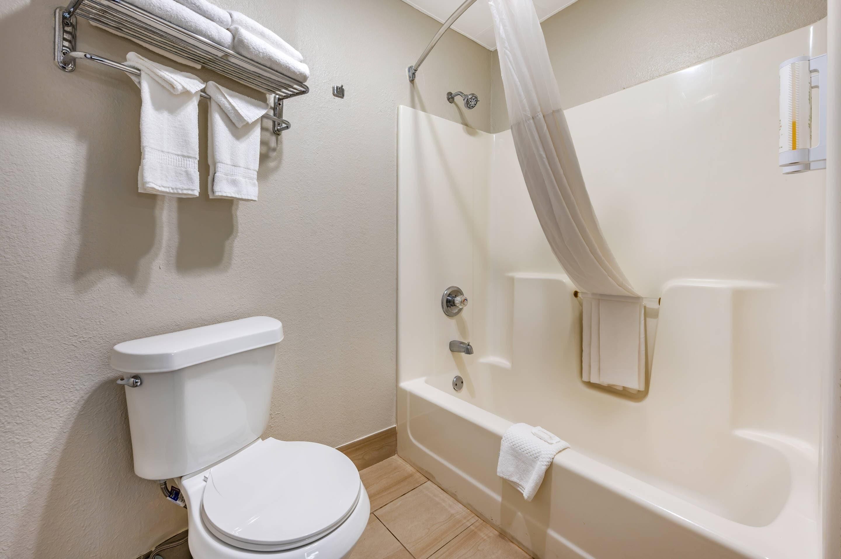 A bathroom with a toilet, a shower with a curtain, and a towel rack with towels.