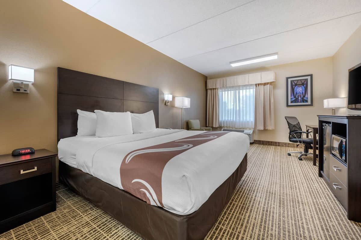 Habitación de hotel con una cama grande, mesitas de noche, un escritorio, una silla, un televisor y una ventana con cortinas.