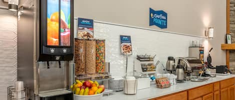 A self-serve breakfast station with a beverage dispenser, cereal, and fruit options.