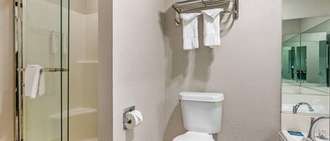 A bathroom with a glass shower enclosure, a toilet, a towel rack with folded towels, and a sink with a mirror.