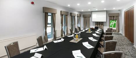 A conference room with a long table, chairs, a projector screen, and a screen displaying 'Holiday Inn'.