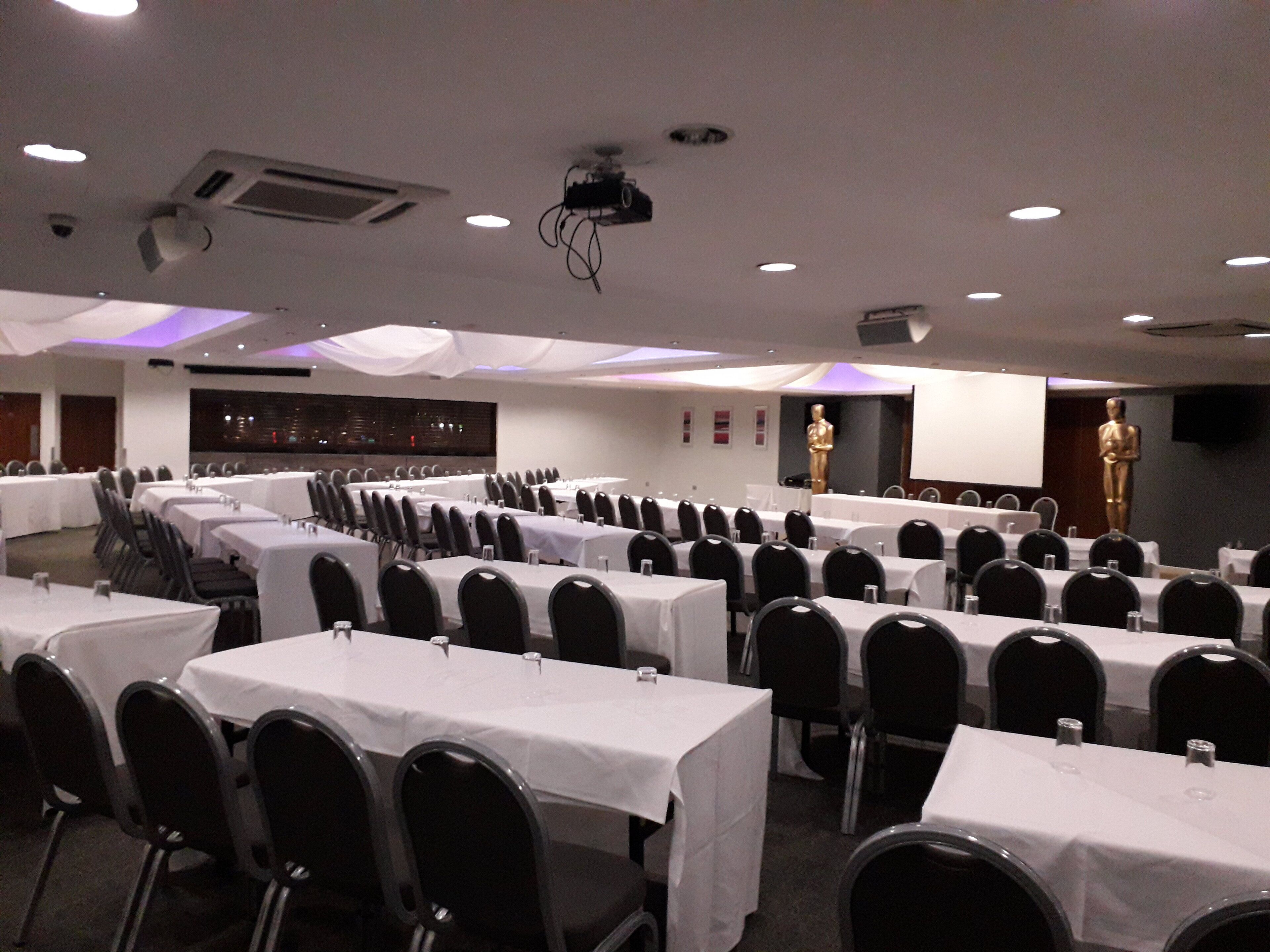 A conference room with rows of tables and chairs, a projector, and a large statue.
