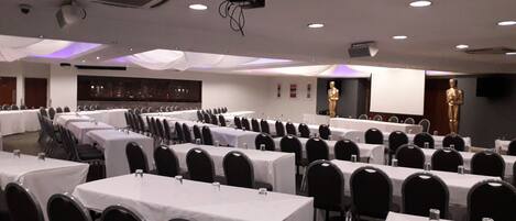 A conference room with rows of tables and chairs, a projector, and a large statue.
