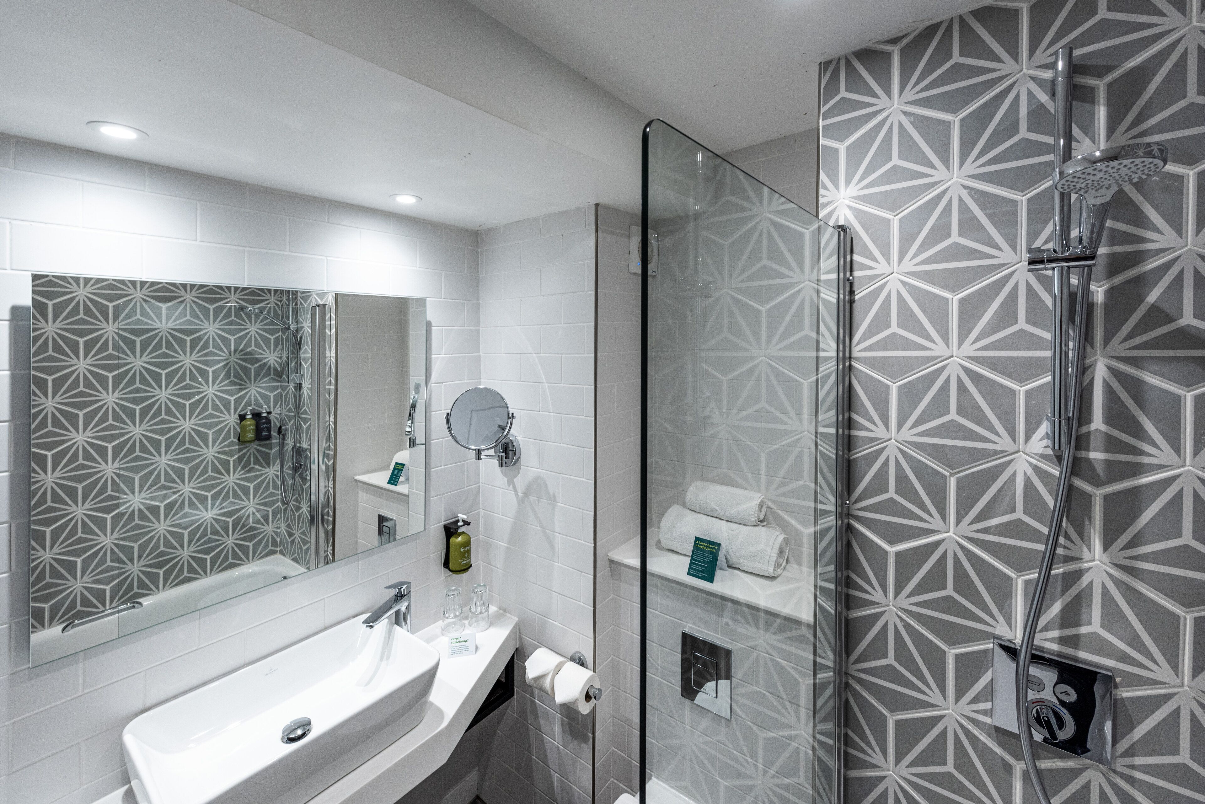 A modern bathroom with a large mirror, a sink, and a shower with a glass door.