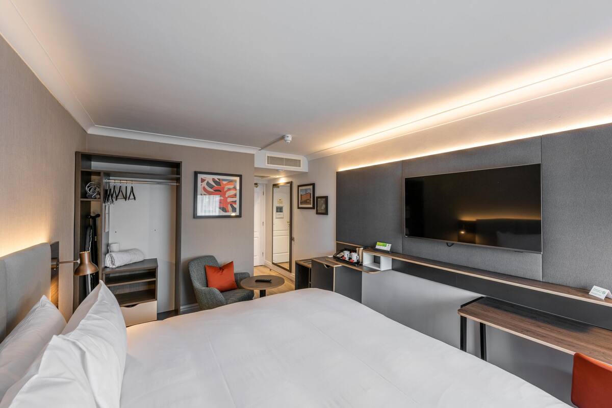Una habitación de hotel moderna con una cama grande, un escritorio, un televisor de pantalla plana, un rincón de descanso y un vestidor.