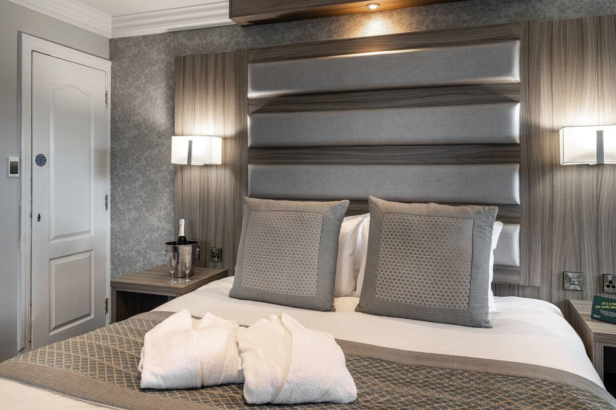 A hotel room with a large bed, two nightstands, a minibar, and a door.