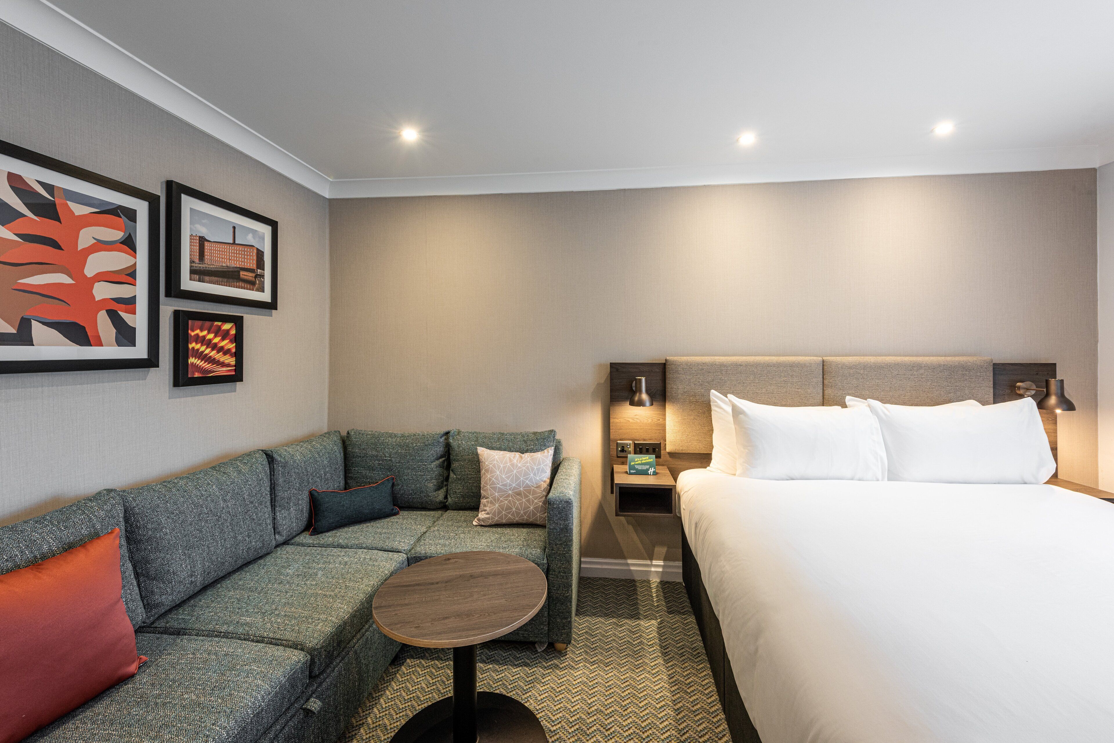 Una habitación de hotel con cama, sofá, una mesita y obras de arte en la pared.