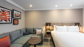 Una habitación de hotel con cama, sofá, una mesita y obras de arte en la pared.