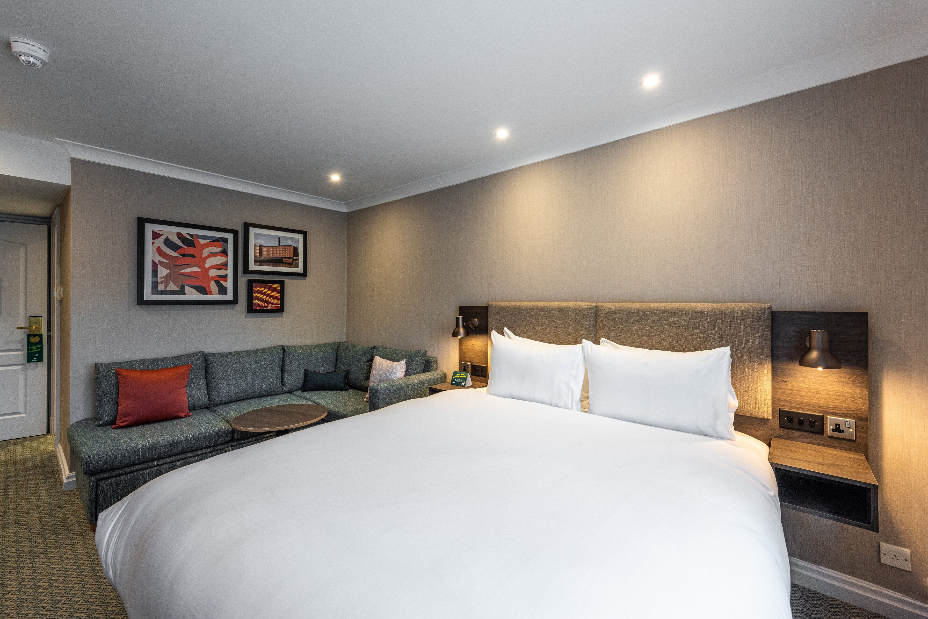 Une chambre d’hôtel avec un grand lit, un canapé, une table de chevet et des œuvres d’art accrochées au mur.