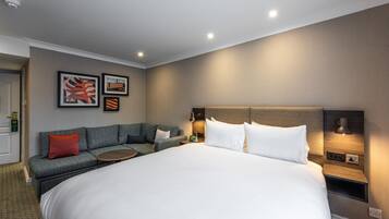 Une chambre d’hôtel avec un grand lit, un canapé, une table de chevet et des œuvres d’art accrochées au mur.