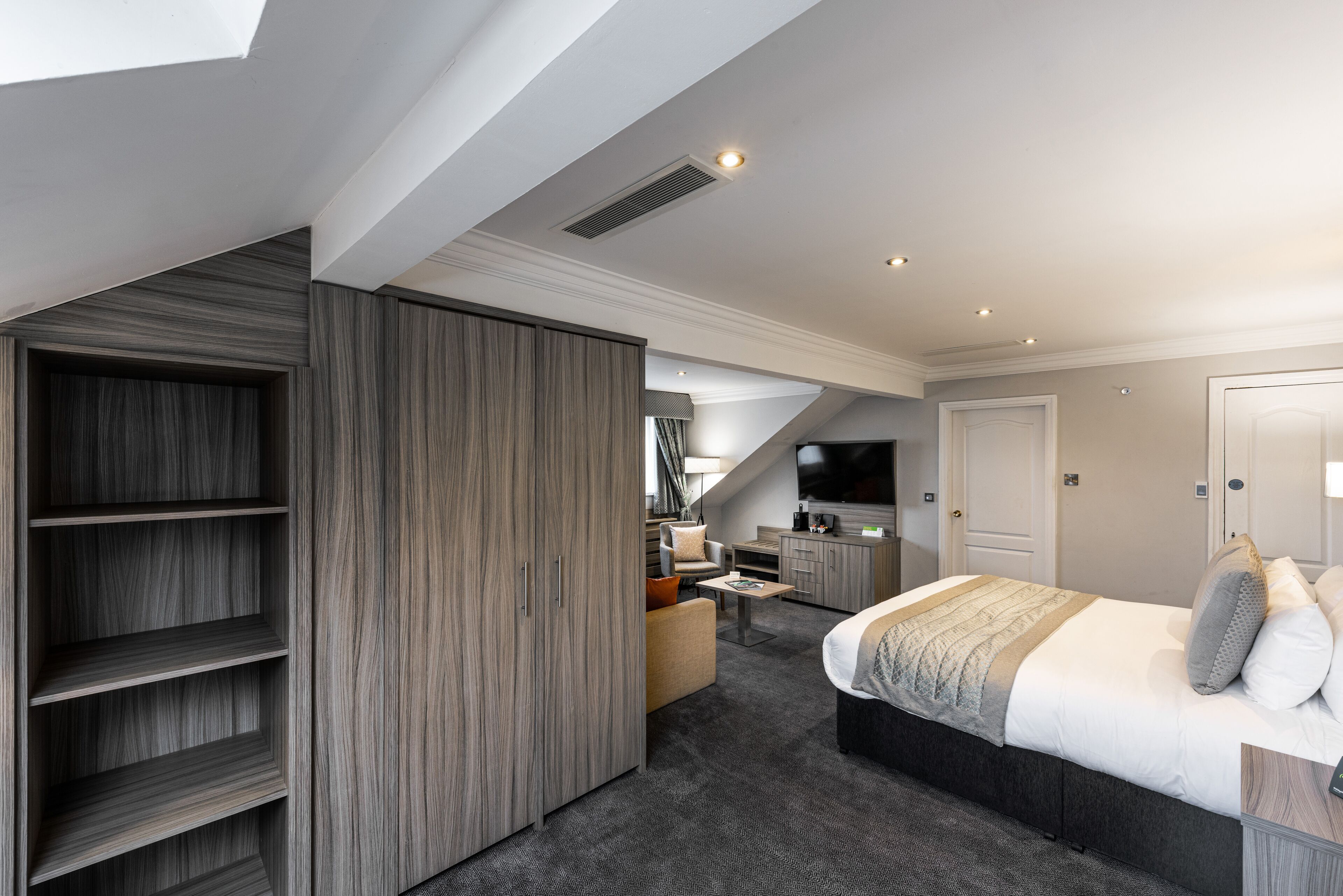 Ein modernes Schlafzimmer mit einem großen Bett, einem Einbauschrank, einer Sitzecke und einem Fernseher.