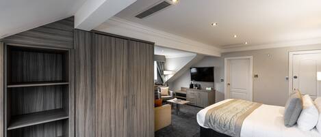 Ein modernes Schlafzimmer mit einem großen Bett, einem Einbauschrank, einer Sitzecke und einem Fernseher.