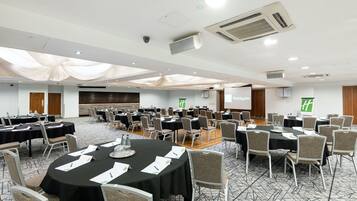 Une salle de conférence équipée de tables rondes, de chaises et d’une scène.
