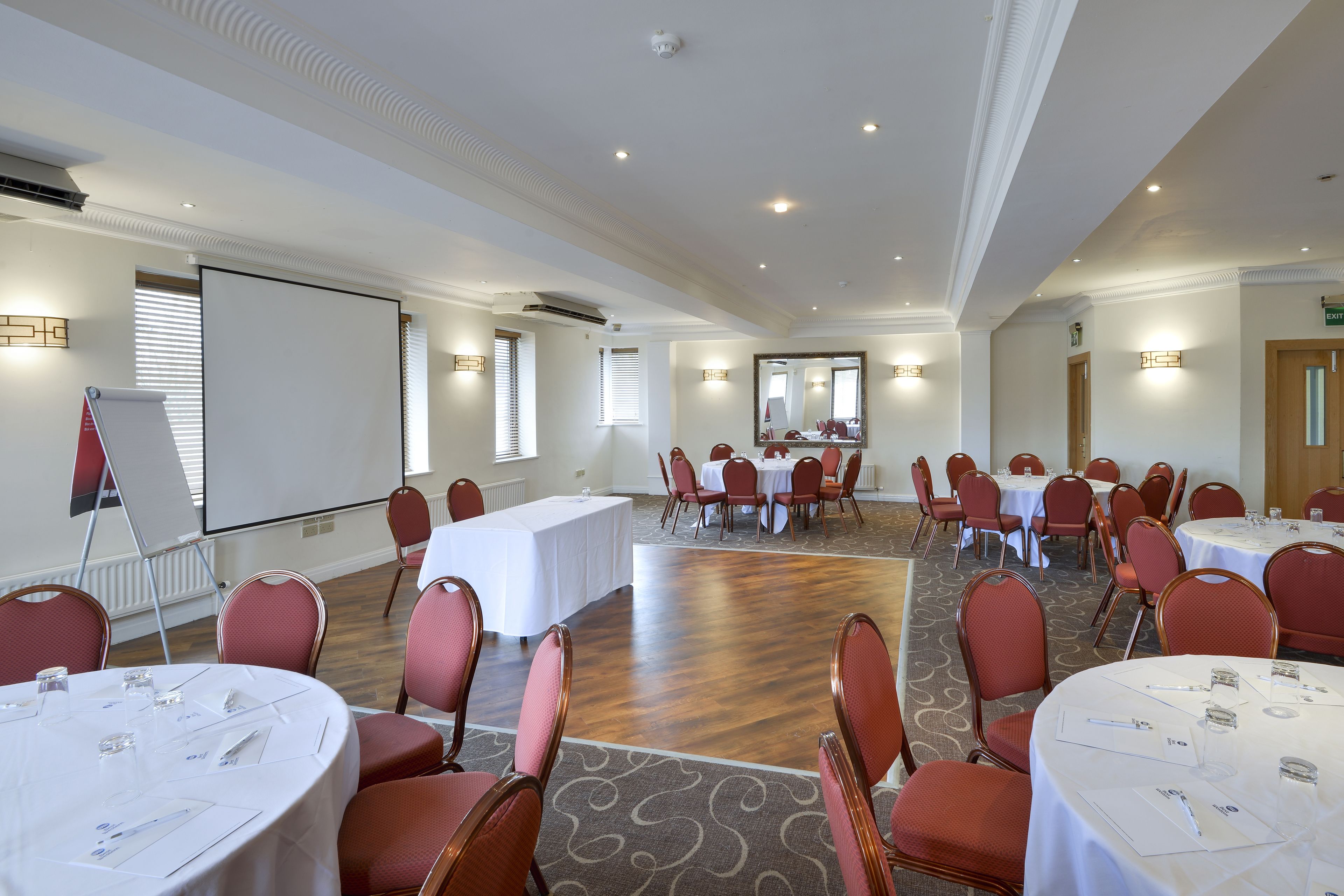 A conference room with round tables, red chairs, and a large screen.