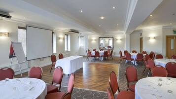 A conference room with round tables, red chairs, and a large screen.