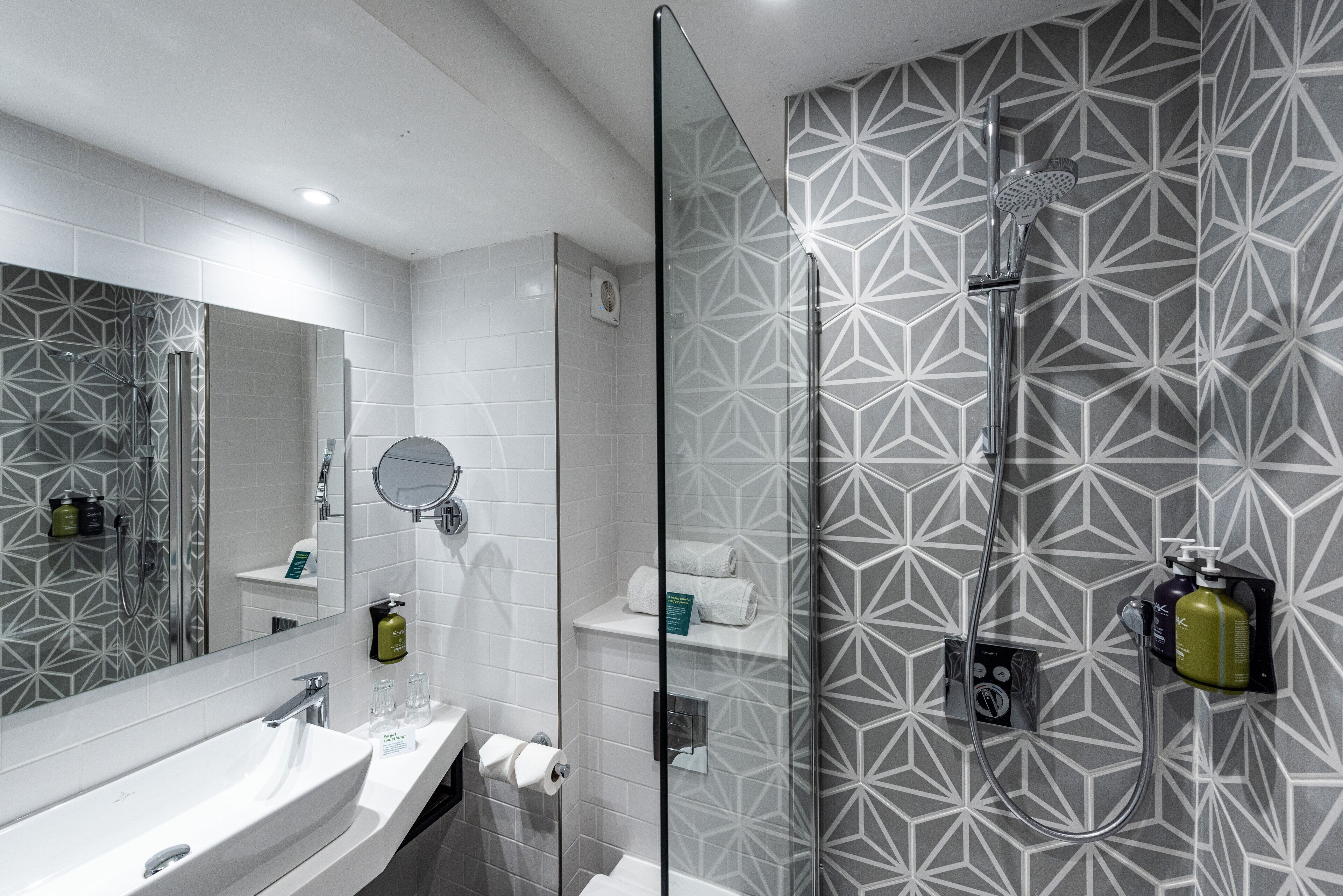 A modern bathroom with a large mirror, a white sink, and a glass-enclosed shower area.