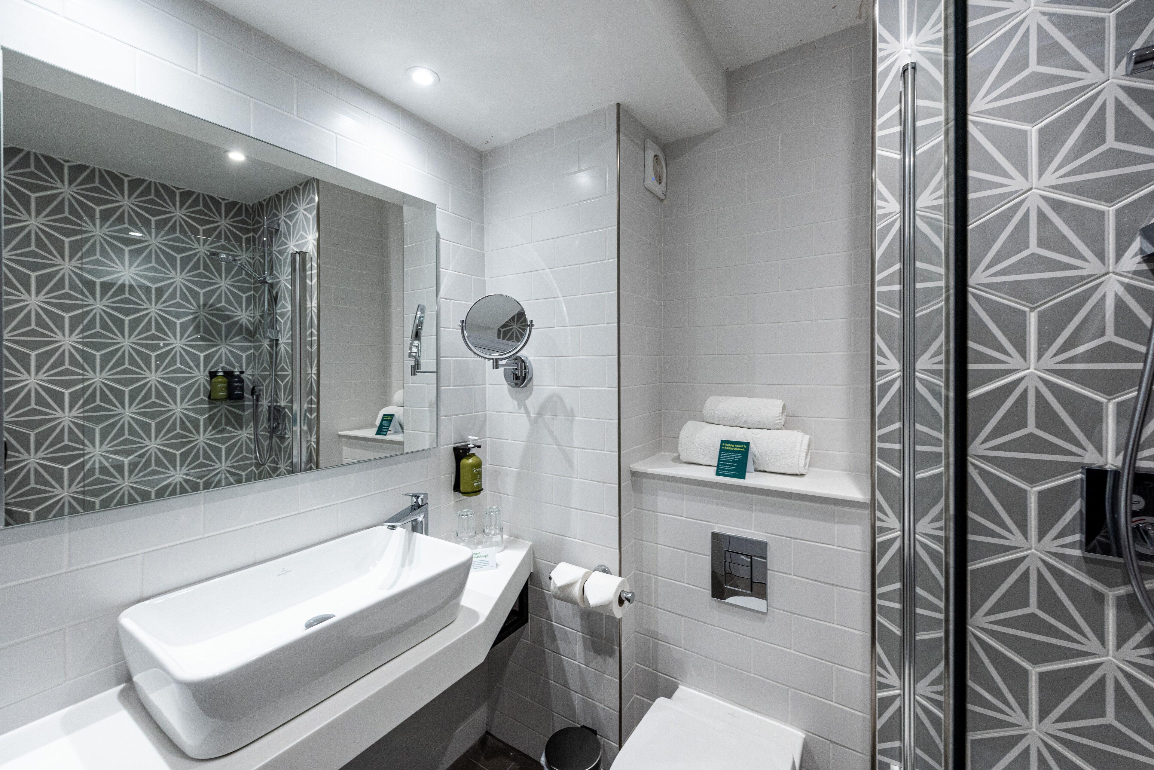 A modern bathroom with a large mirror, white sink, and a shower area.
