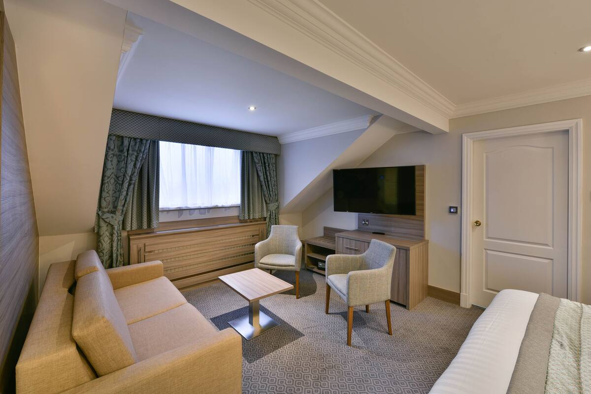 A hotel room with a sofa, armchair, TV, and a bed.