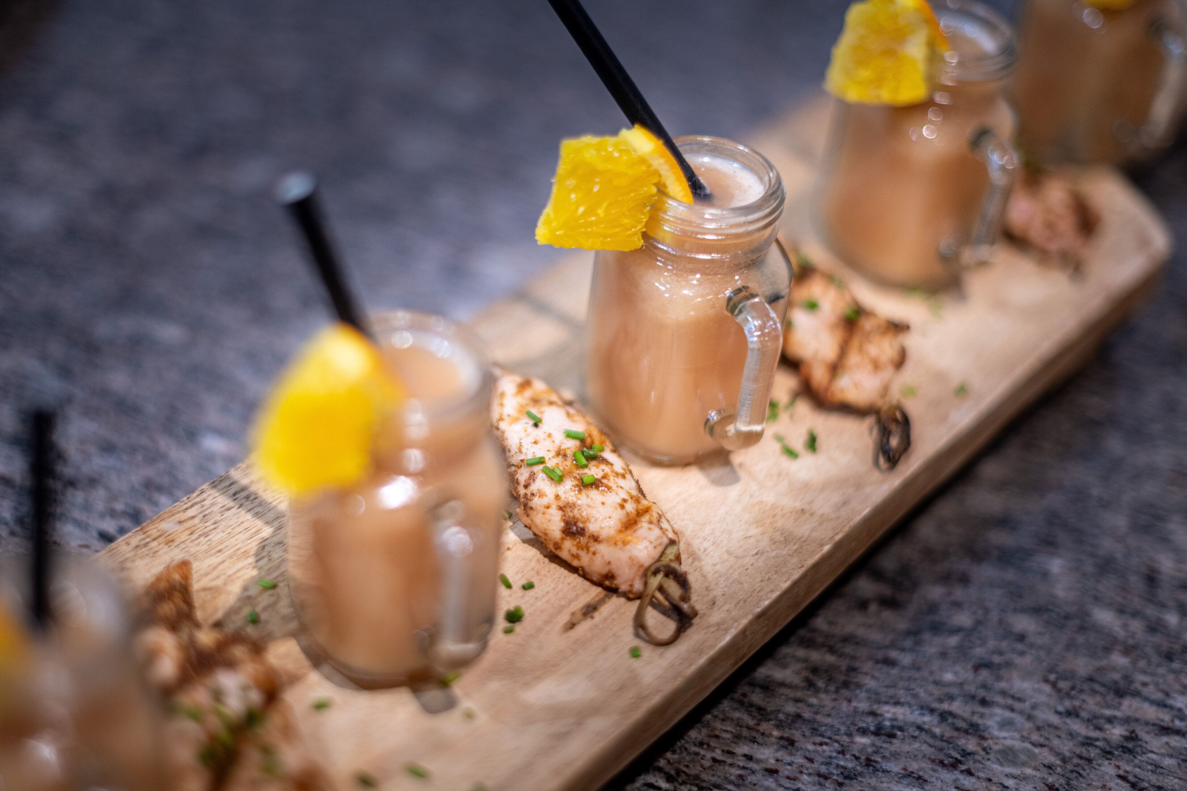 A wooden serving board with three glass mugs of iced coffee, garnished with orange slices and herbs.