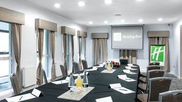 A conference room with a long table, chairs, a projector screen, and a large window with curtains.