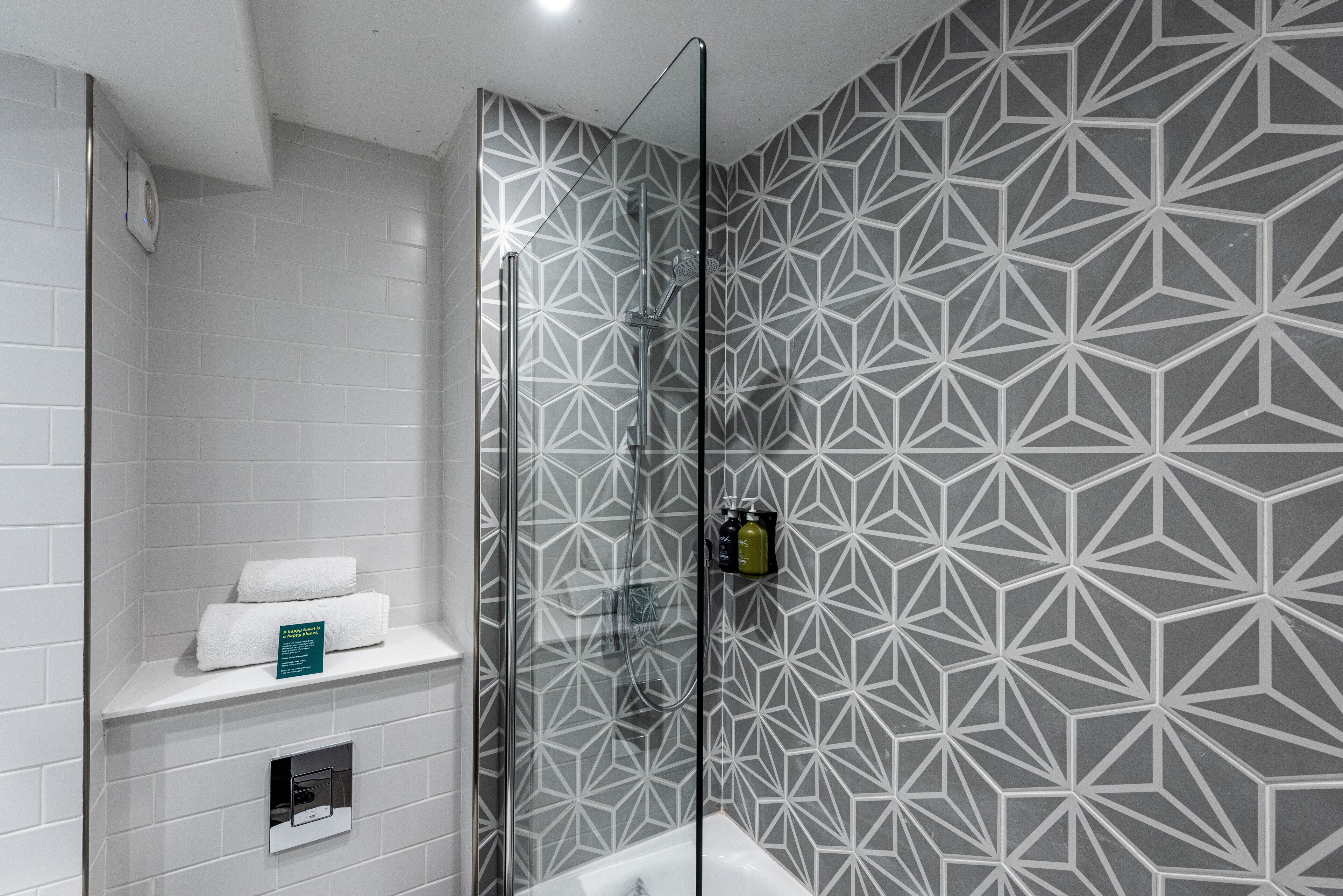 A modern bathroom with a geometric patterned wall, a glass shower enclosure, and a white sink with a towel rack.