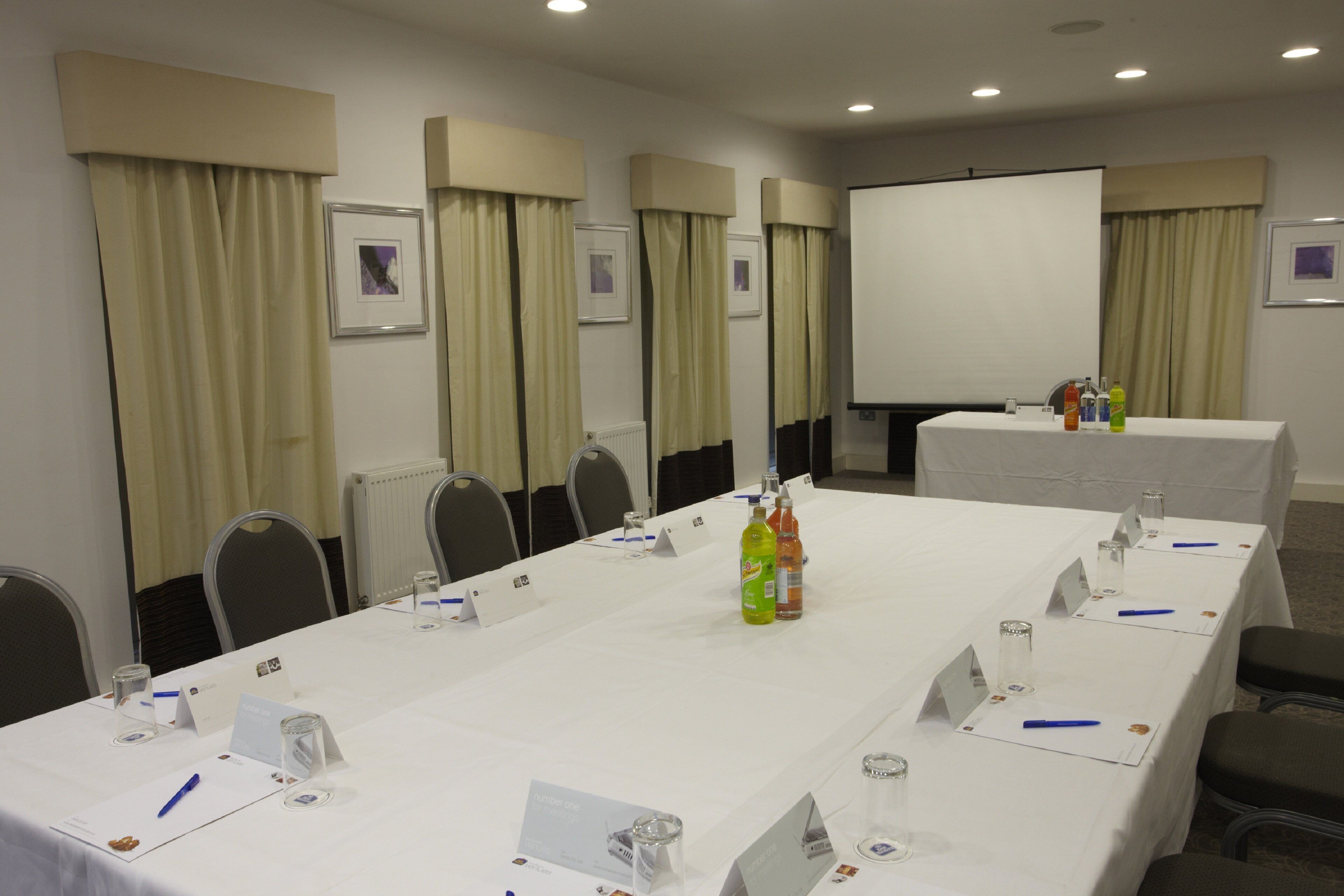 A conference room with a long table, chairs, nameplates, and a projector screen.