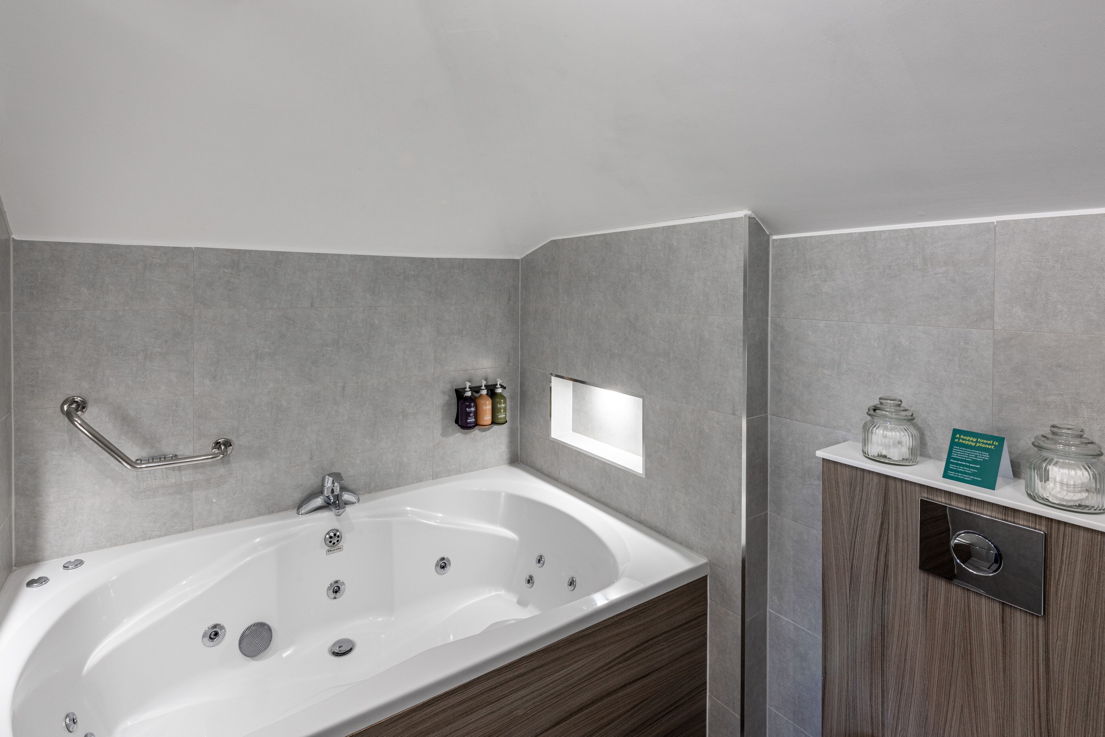 A modern bathroom with a freestanding bathtub, a handrail, and a vanity with a mirror and storage jars.
