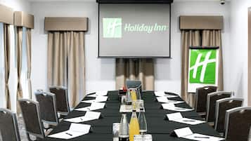 A conference room with a long table, chairs, a projector screen, and a Holiday Inn logo.